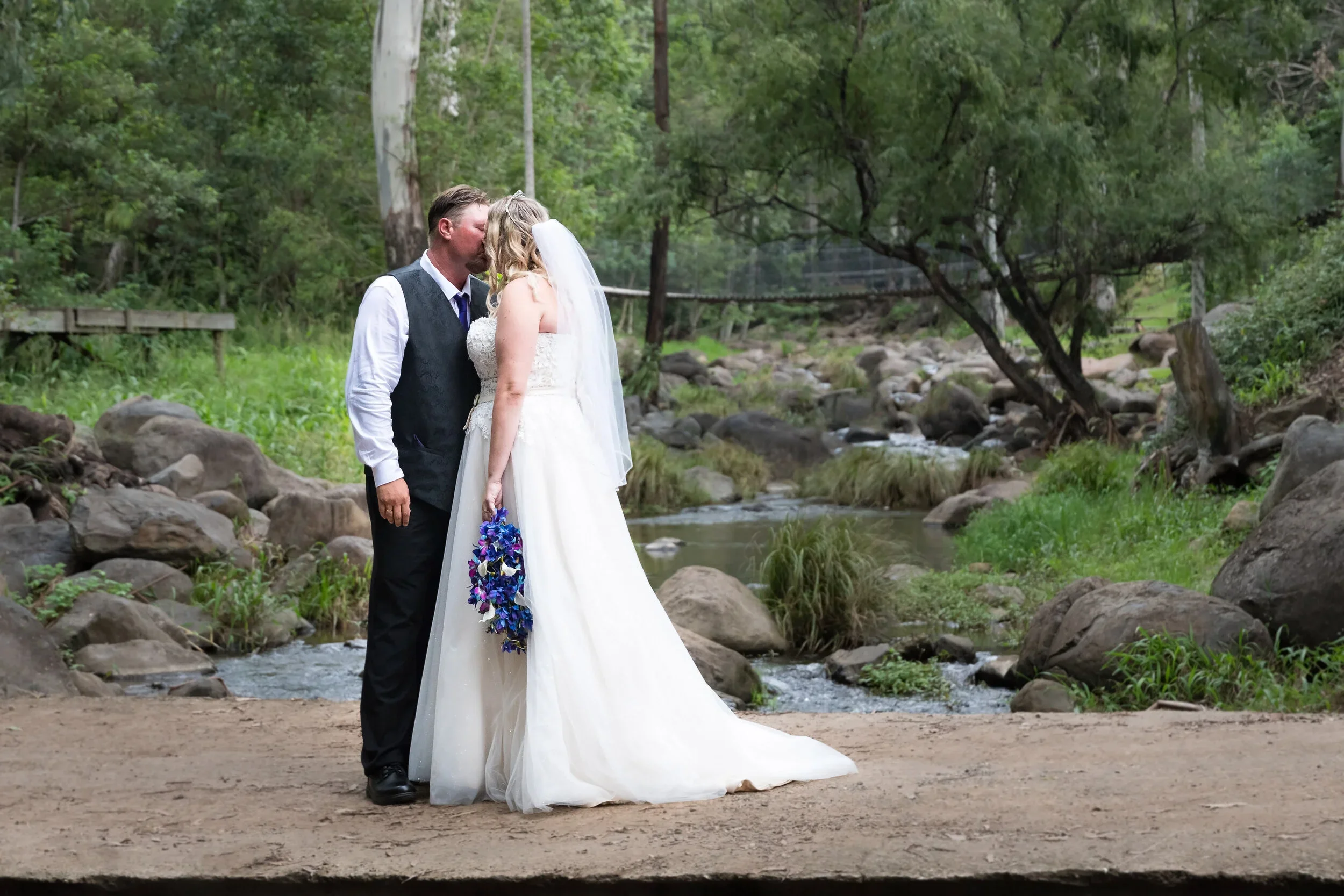 A bride and groom sharing a kiss by a flowing creek surrounded by lush rainforest at a tamborine mountain wedding in the Gold Coast hinterland, captured by Scott Hardy Photography
