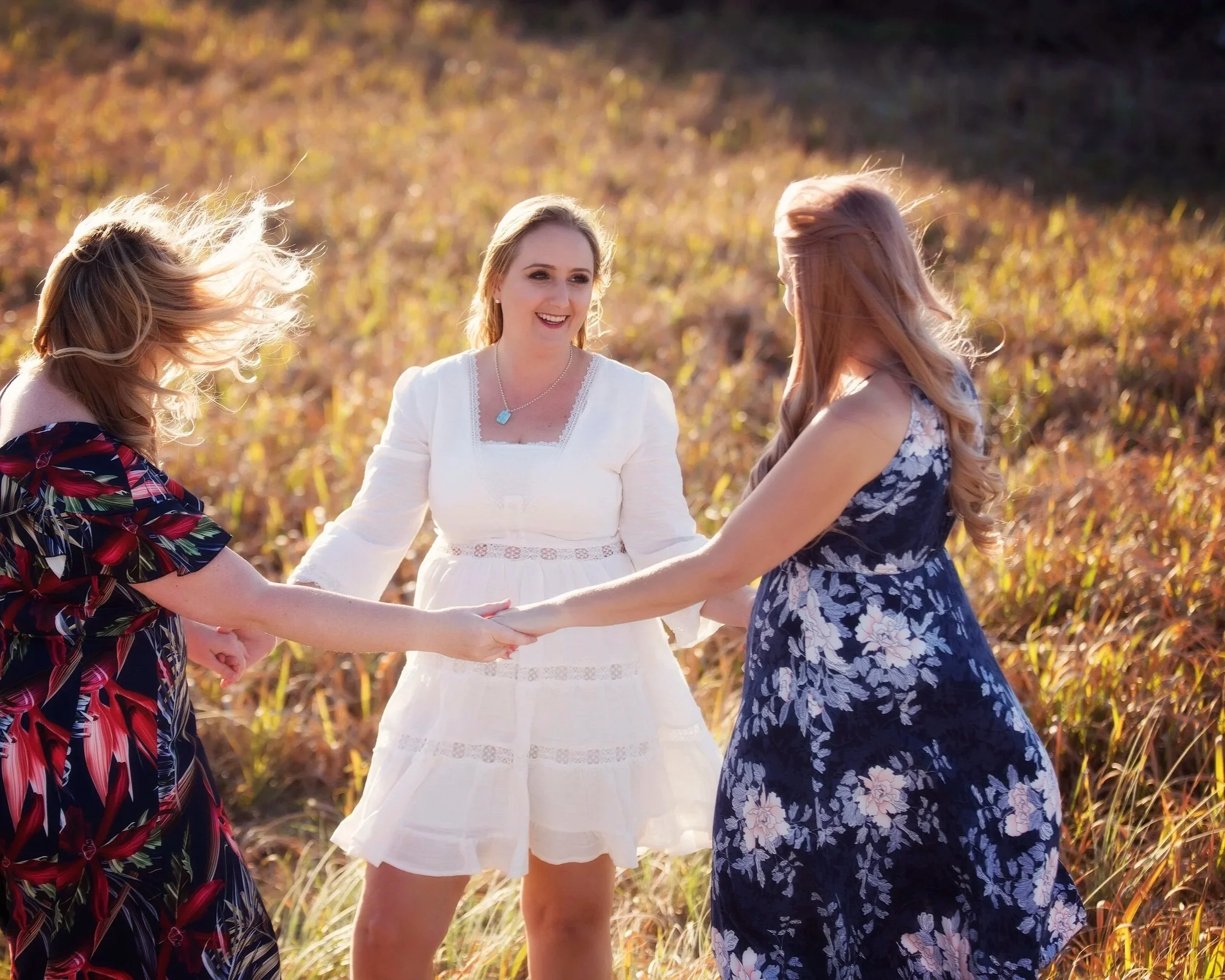 Three women holding hands and smiling in a field of tall grass