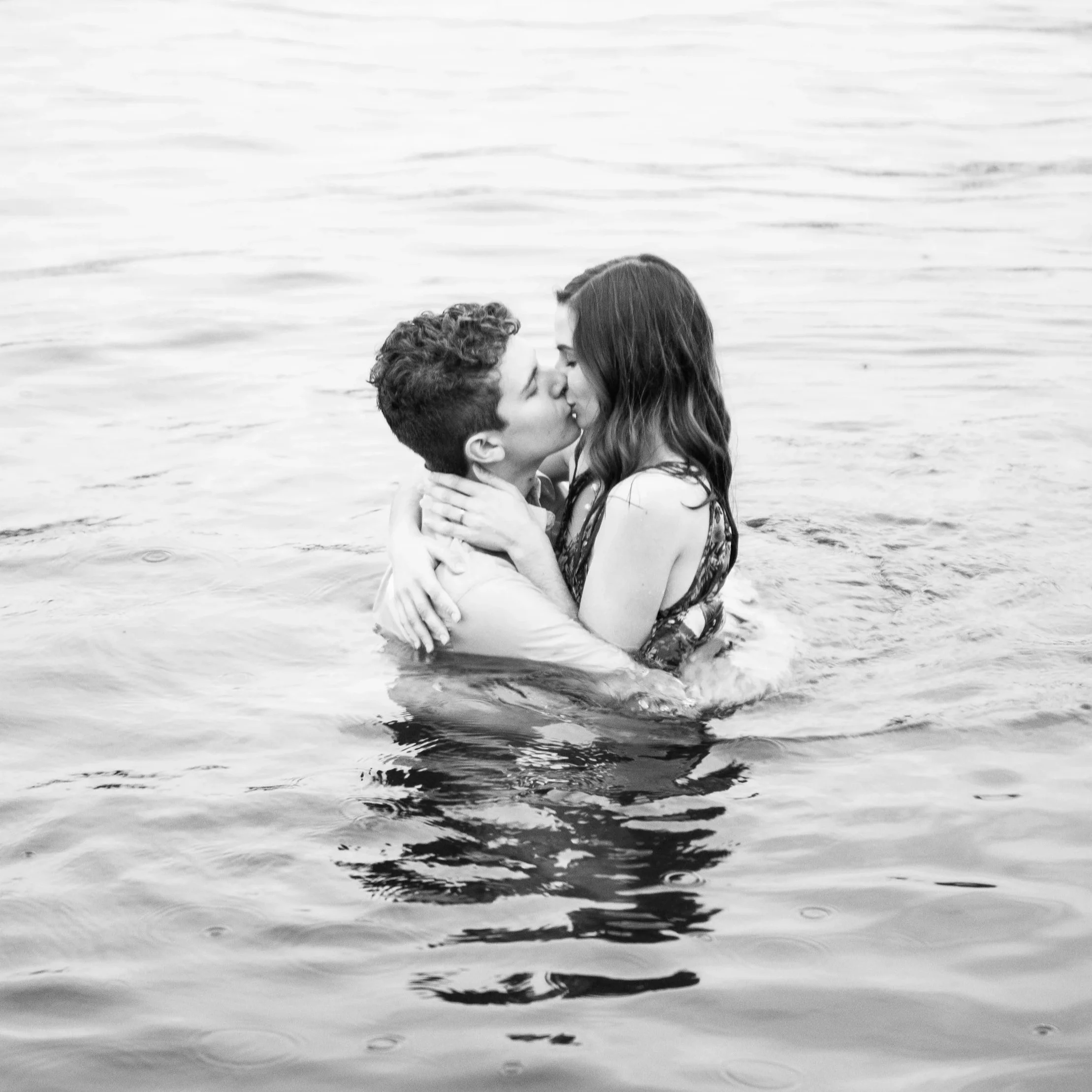 a black and white photo of a couple kissing while submerged in a lake