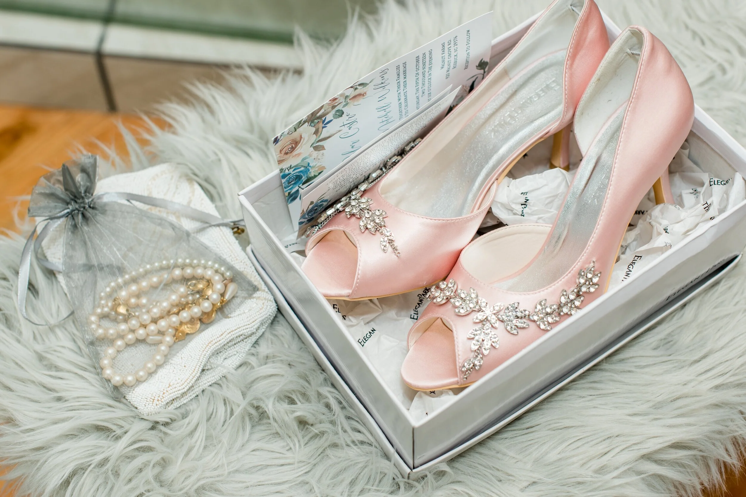 A box of bridal details, including pink shoes, jewelry, and an invitation suite