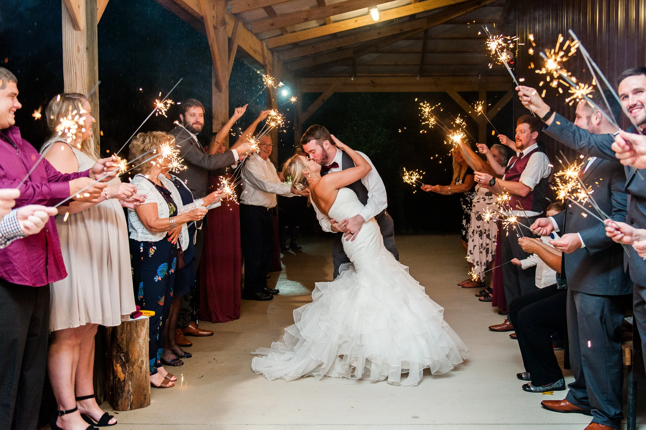 A bride and groom dip and kiss in the middle of rows of people holding sparklers