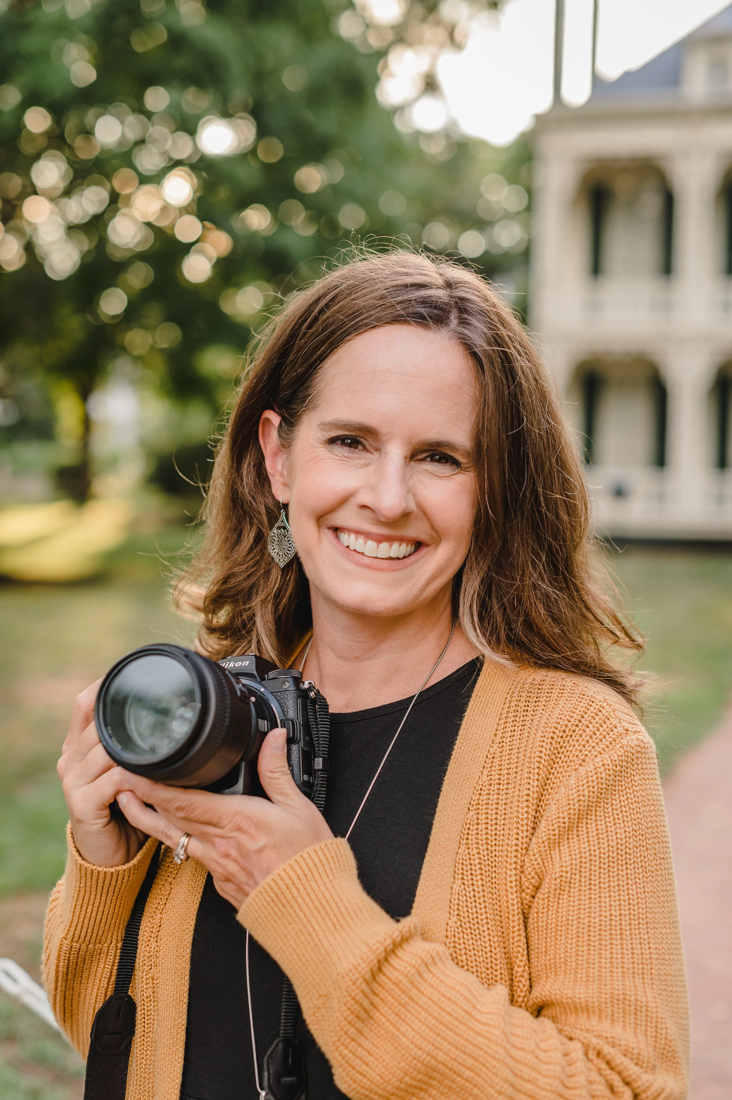 A photographer smiles at the camera while holding her own camera.