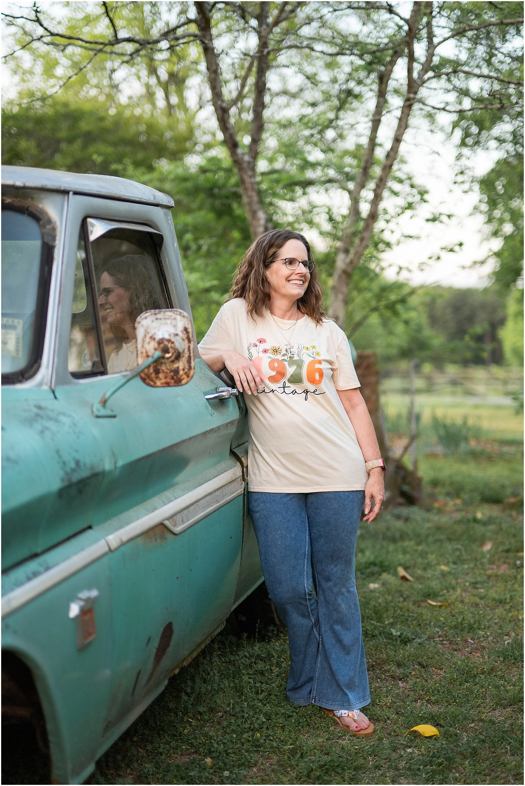 Lady born in 1976 wearing a vintage 1976 tshirt leaning against a vintage green pickup truck