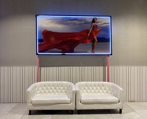 Two white, tufted sofas under a lit photo display. The photo features a woman wearing a flowing red dress, standing in a desert landscape.