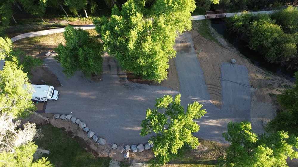 Approved River B/C Camp overview from above, showing gravel RV pads, trees and the small bridge at Woods and River RV Park.