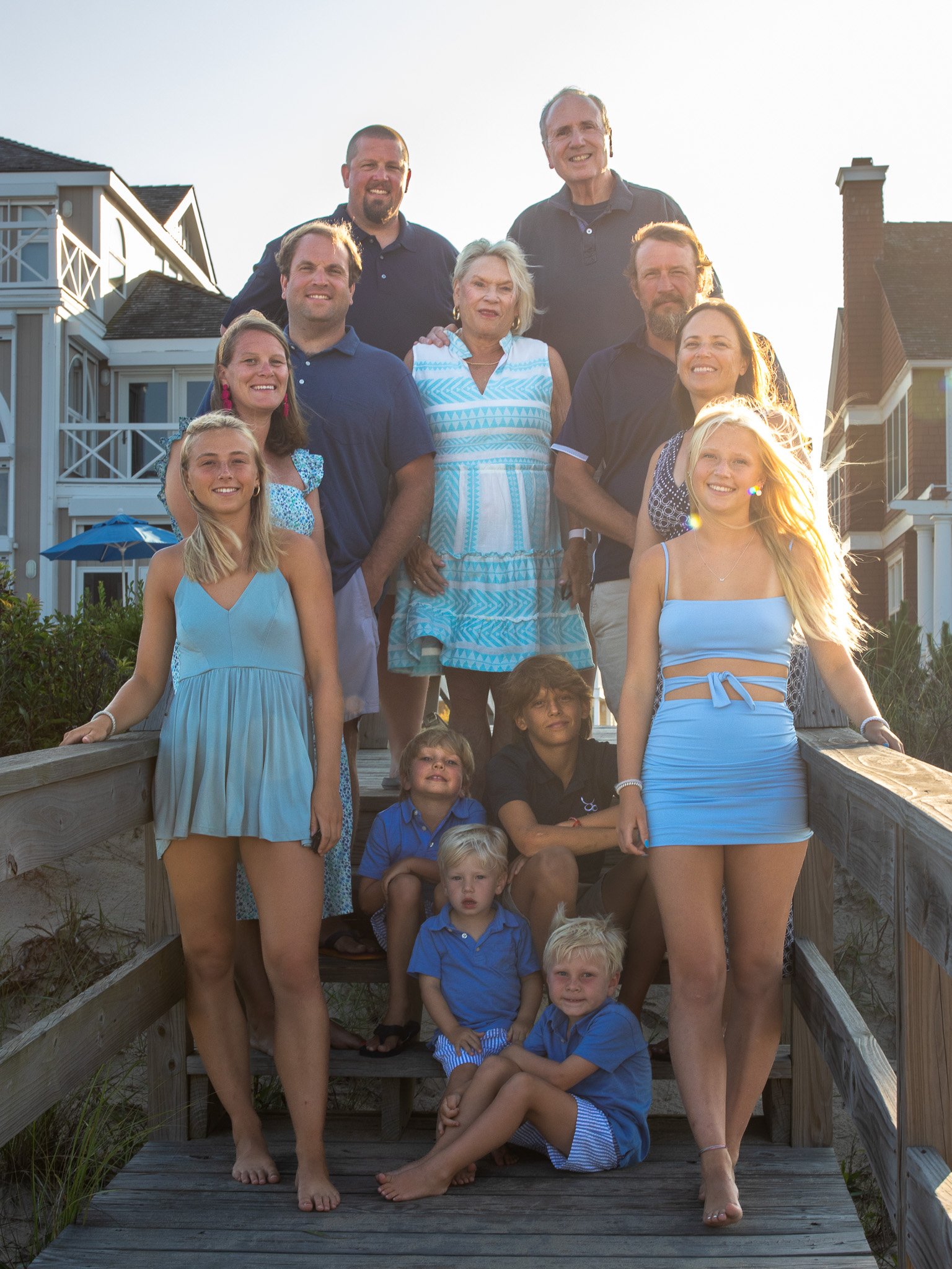Family photo on outdoor wooden walkway, with people in blue and white attire, beach houses in background.