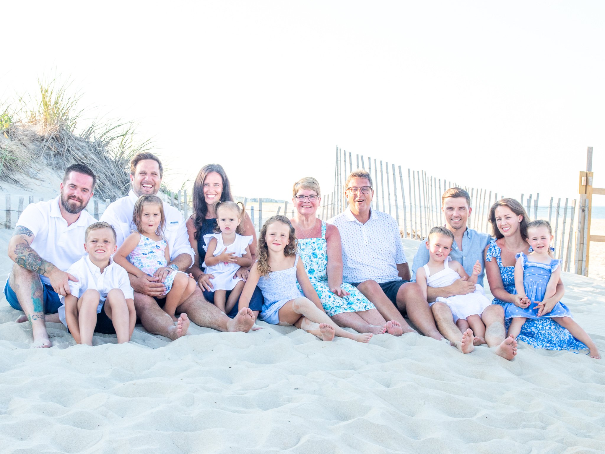 Family group photo on sandy beach with wooden fence and grass in background.