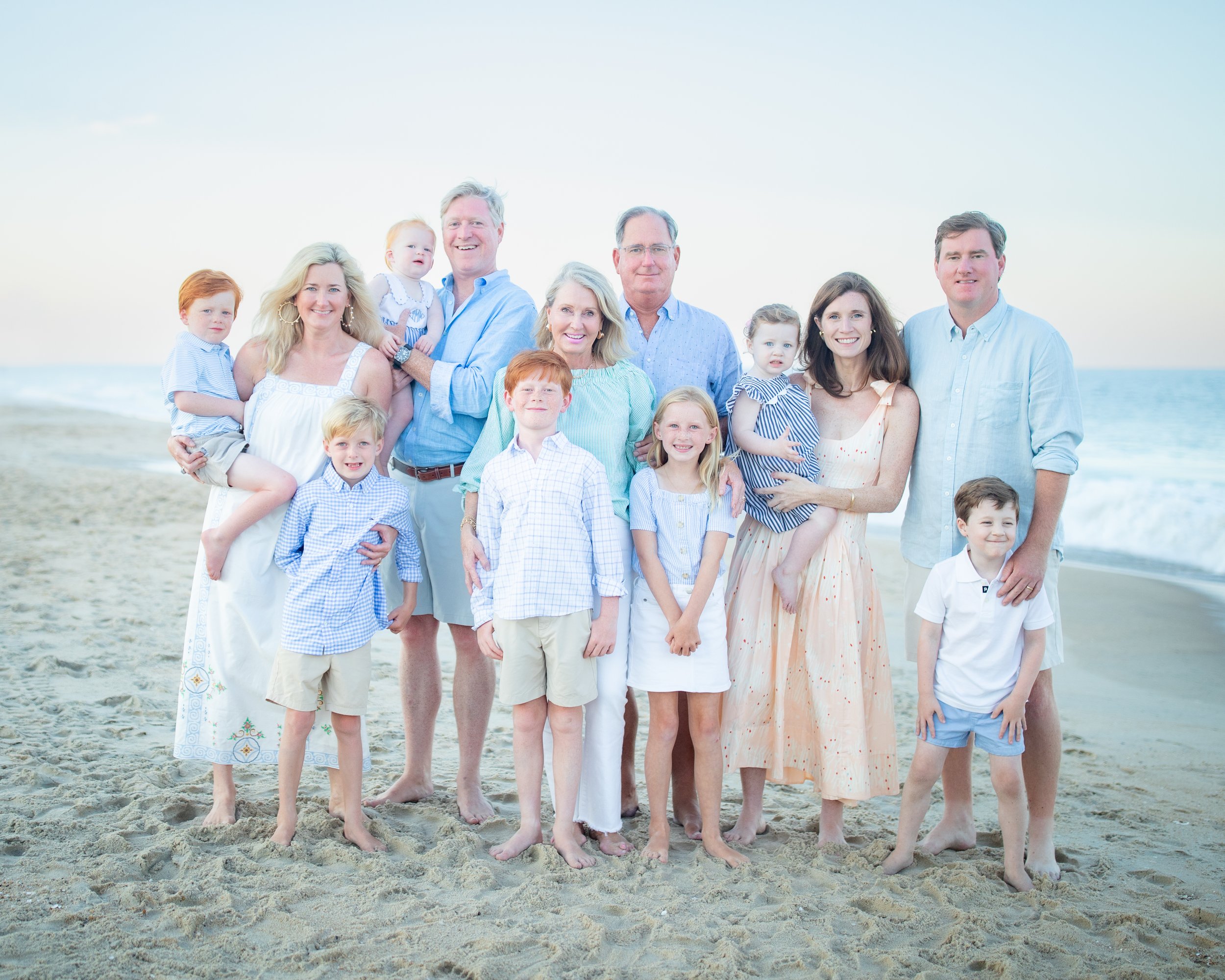 Family portrait on a beach with ocean in background, featuring adults and children in casual summer clothing.