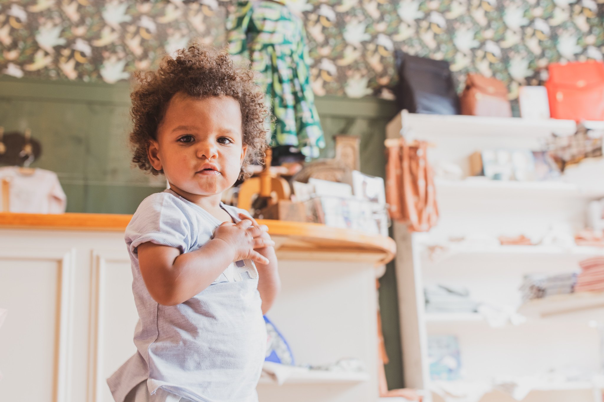 Child in a room with shelves, wearing a light blue shirt.