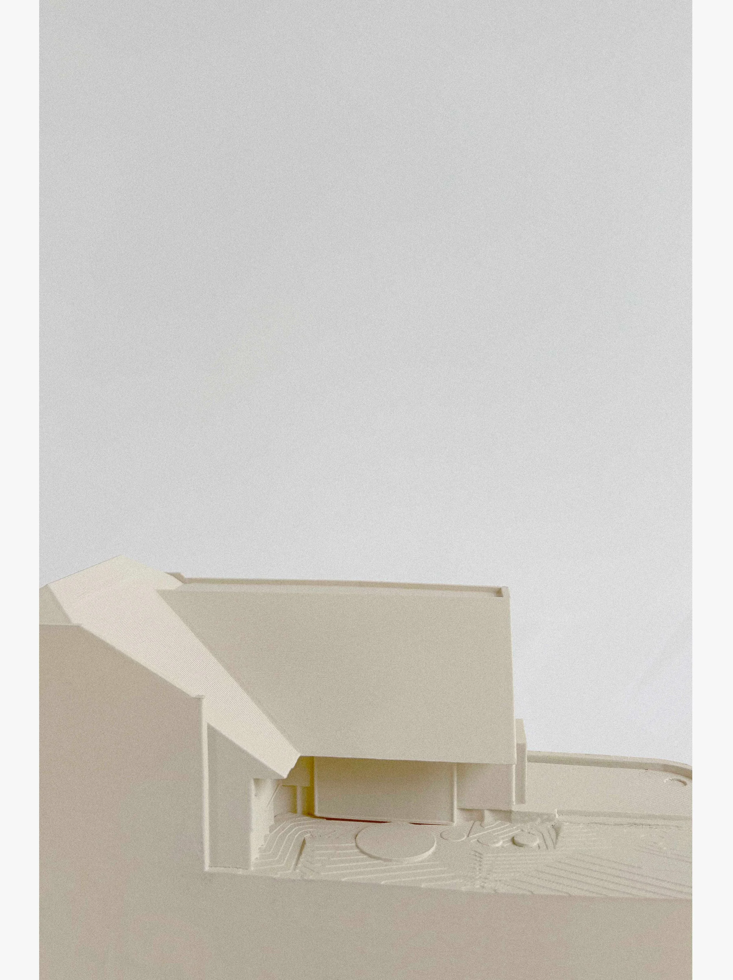 Architectural model of a modern building with a curved roof and surrounding landscape features.