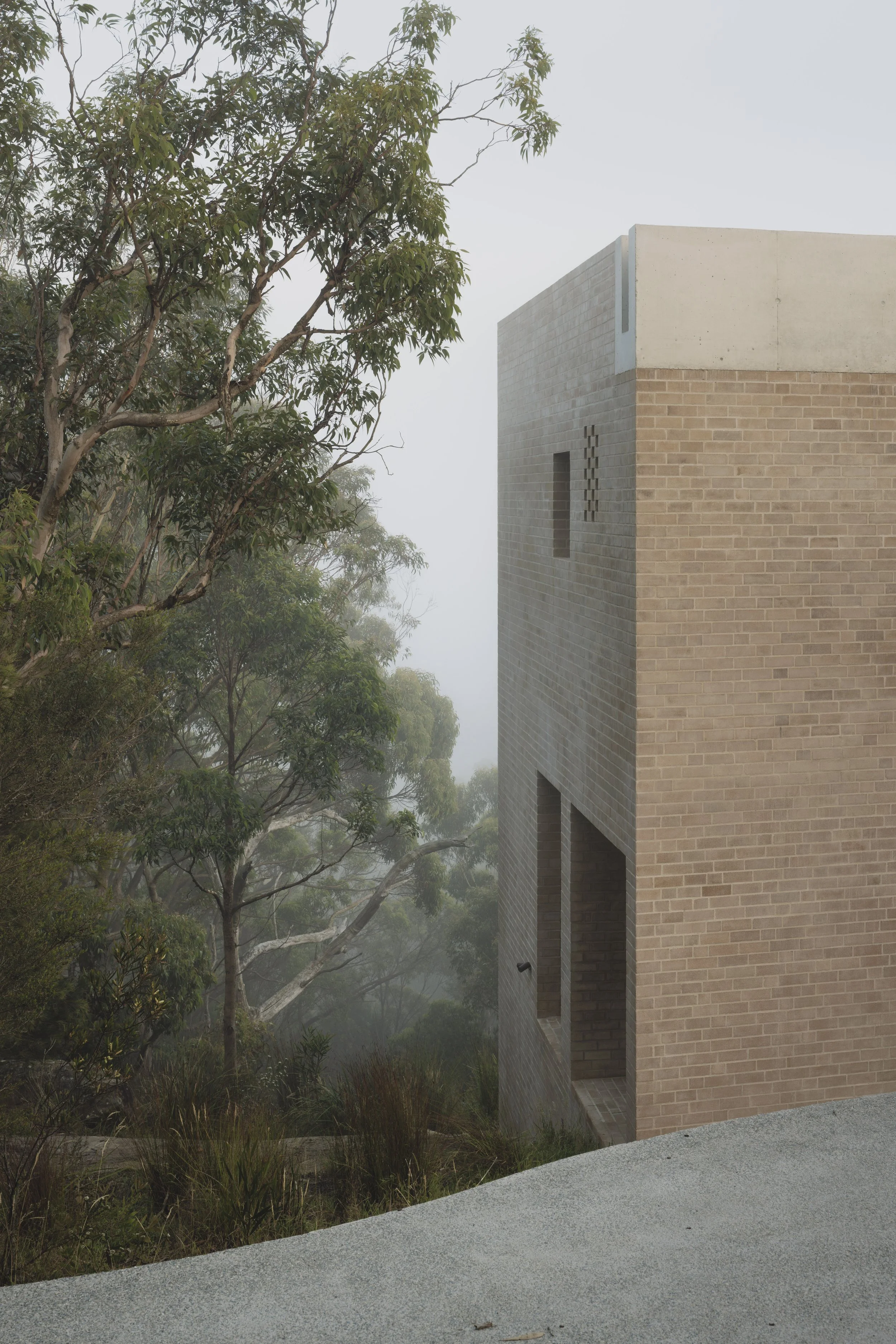 A modern brick building with rectangular windows, surrounded by trees and foggy weather.