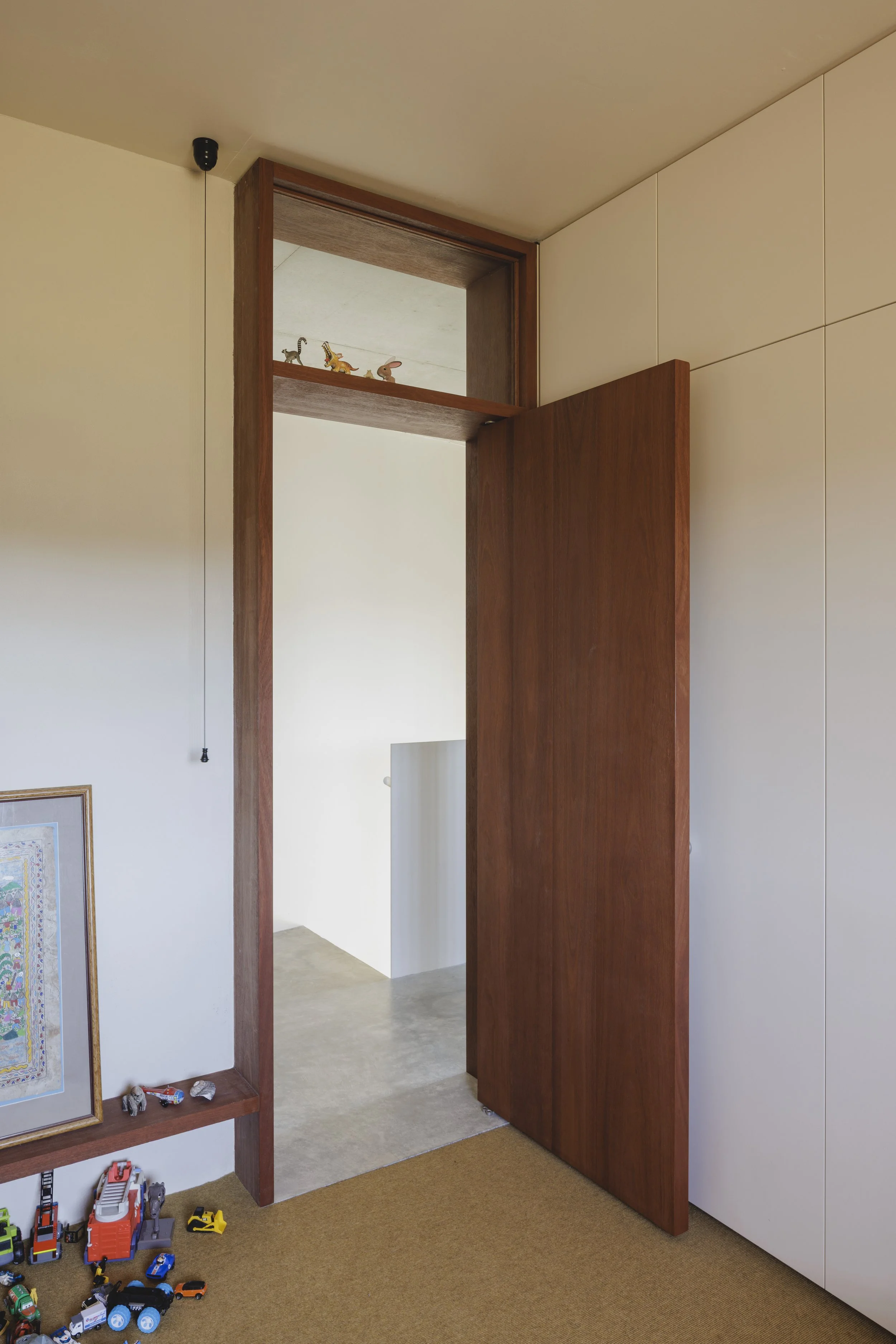 Part of a hallway with toys on a carpeted floor, a framed artwork, and a wooden architectural feature leading to another room.