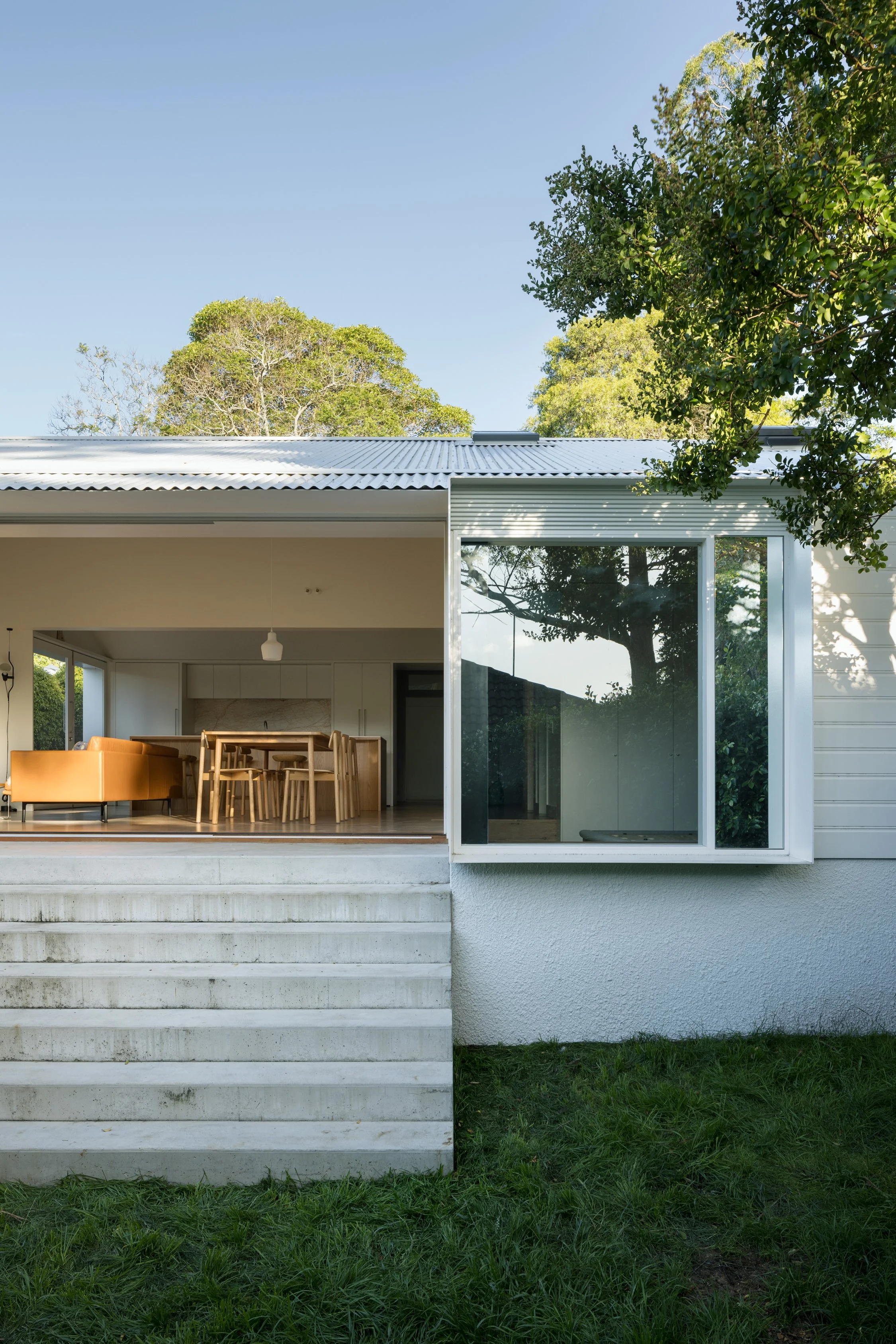 Modern house with an open living area, visible through large windows, set on a grassy terrain with trees in the background.