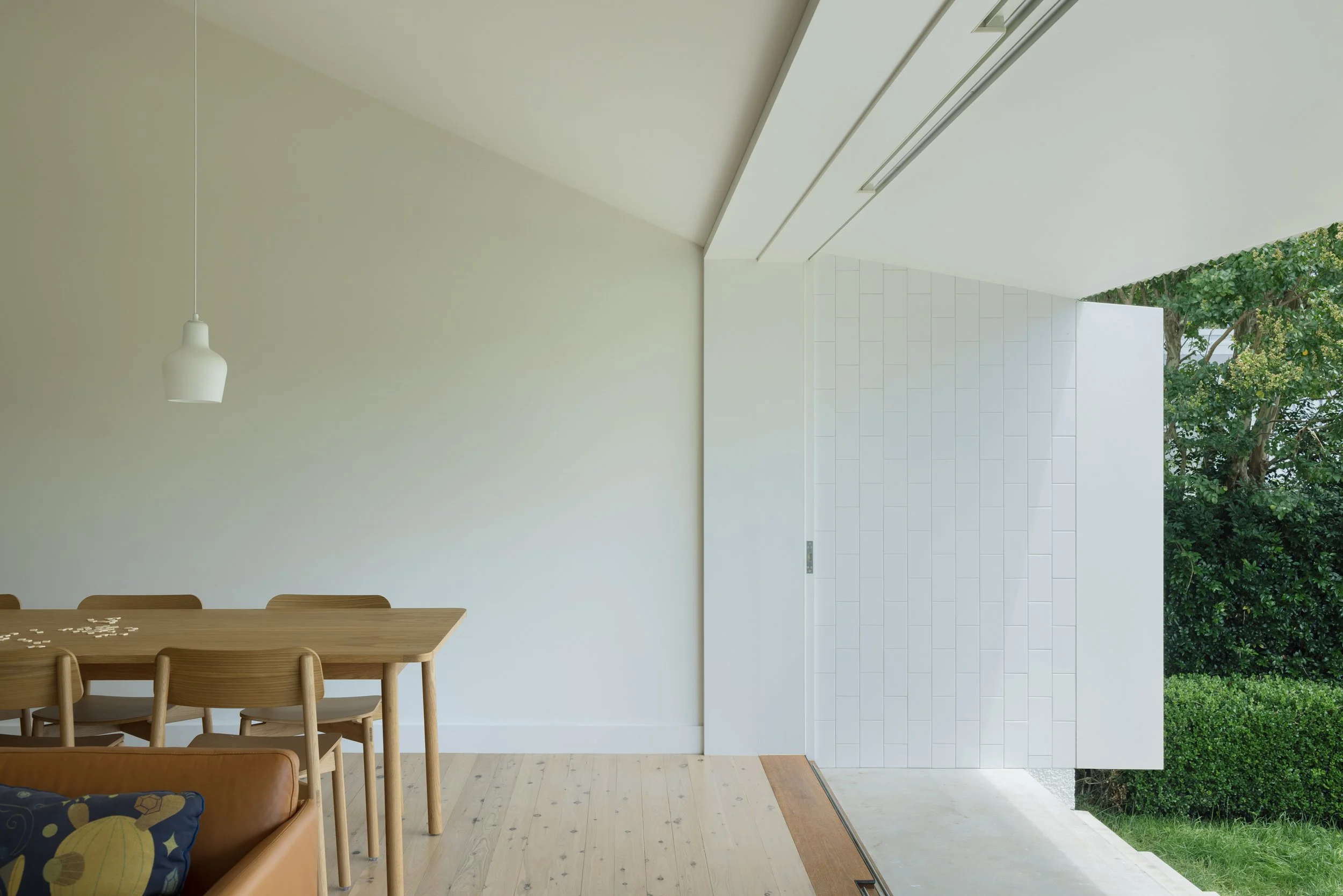 Interior of a modern home with a dining area and large sliding glass door opening to a green outdoor space.