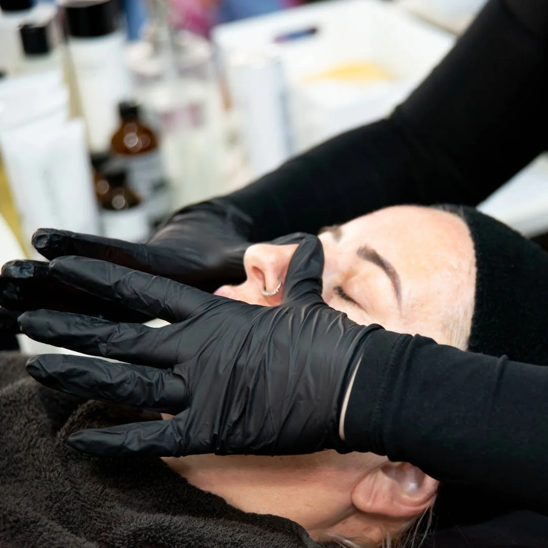 A person receiving a facial treatment from a professional wearing black gloves in a clinical setting.