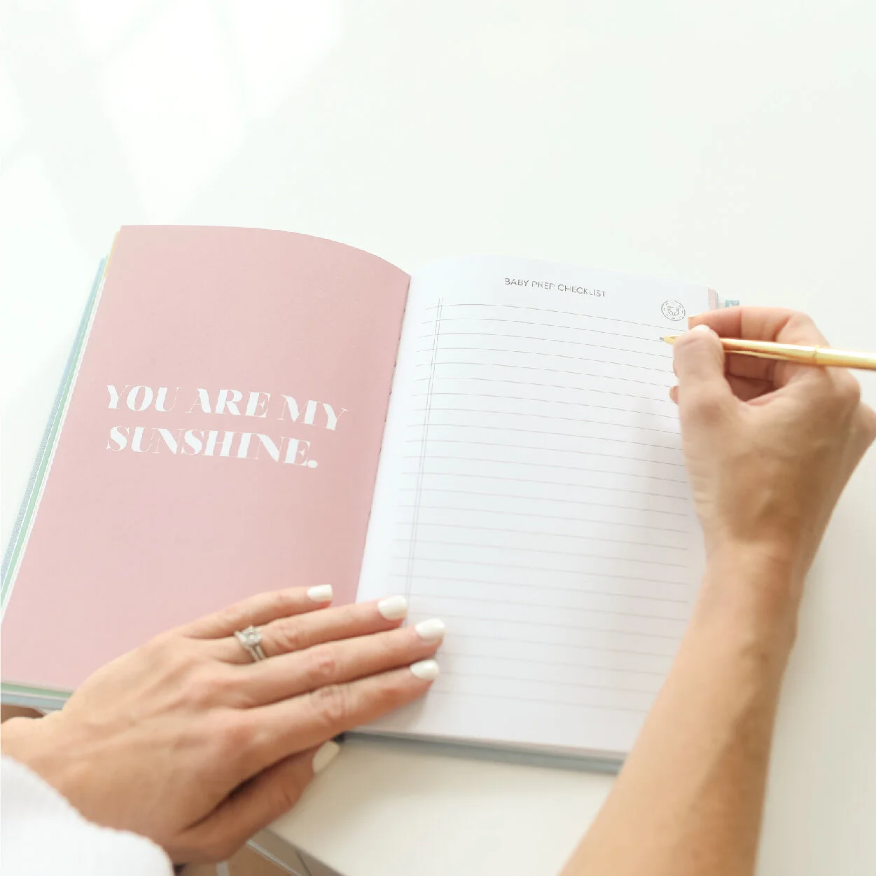 A woman's hands filling out a page in The Pregnancy Journal with a quote on the adjacent page reading "you are my sunshine".