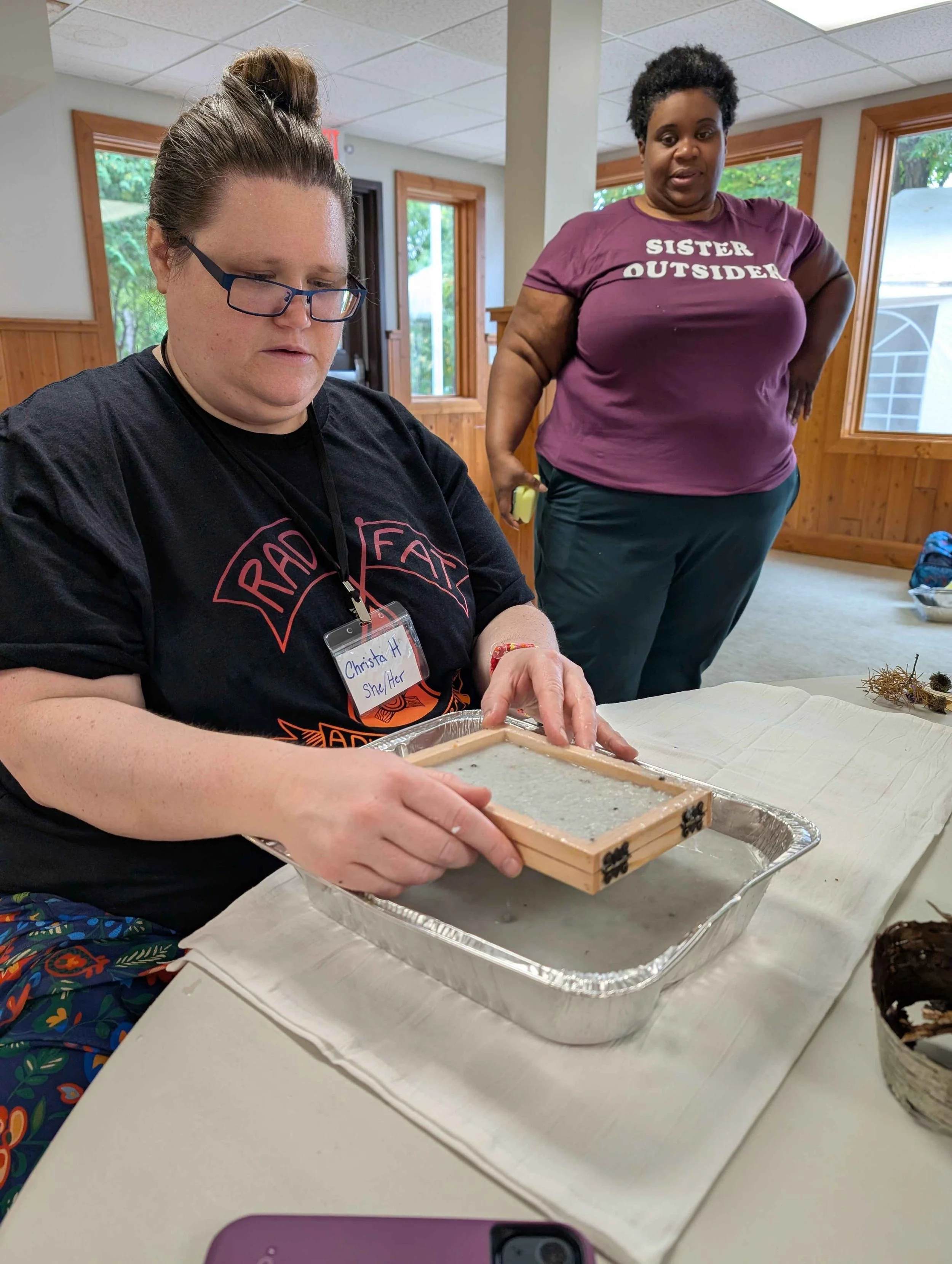 A camper learns paper-making while the instructor looks on in the background.
