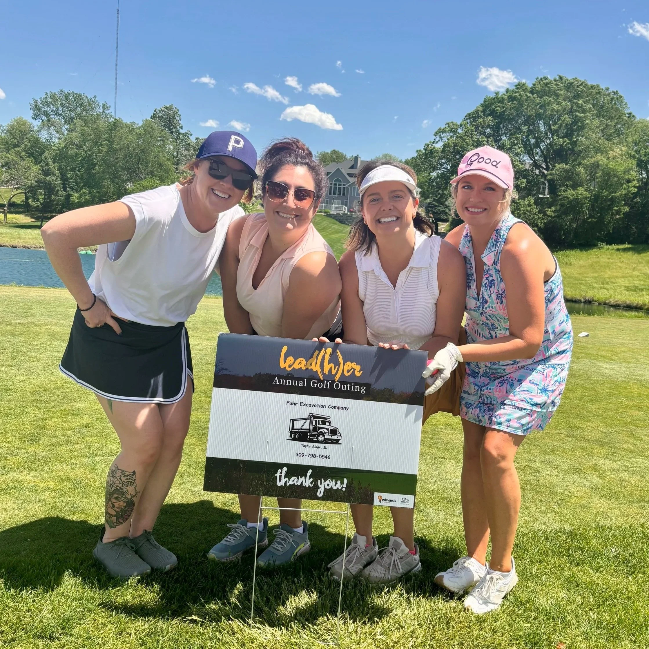 Four female golfers pose with a hole sponsor sign at a charity golf tournament.