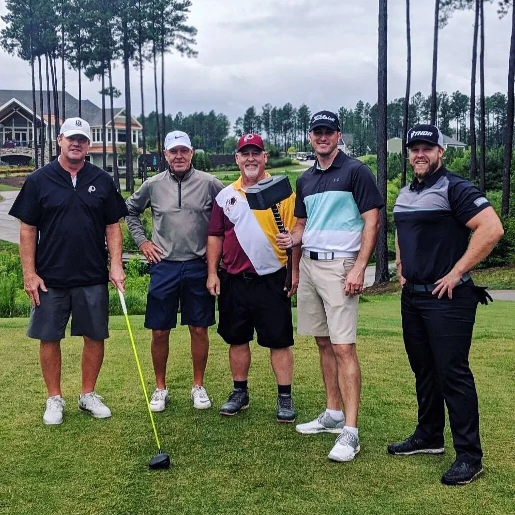 Four golfers and a long-drive professional pose at a charity golf event.