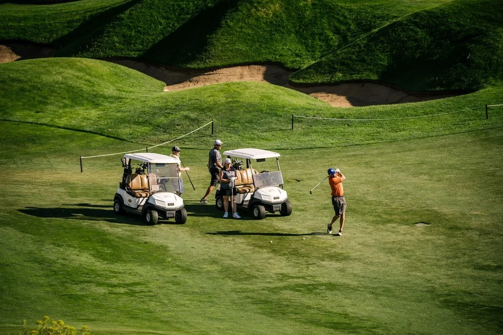 One golfer hits a shot while three others wait their turn at a charity golf tournament.