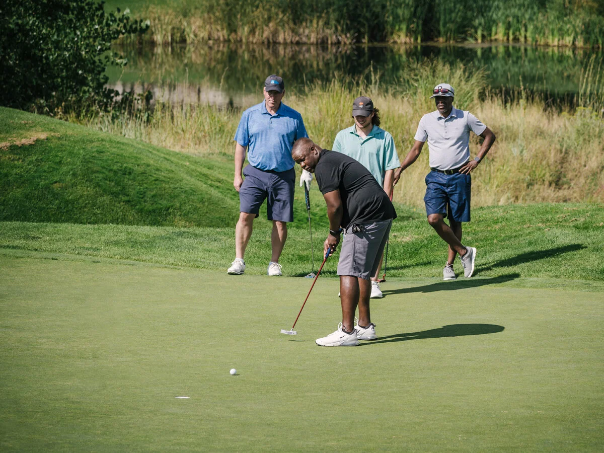 A golfer putts on the practice green while three others watch during a golf putting contest.