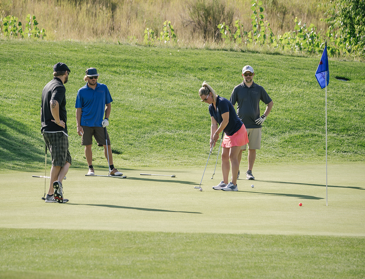 A woman putts and three men watch as part of a charity golf tournament powered by GolfStatus' tournament management software.