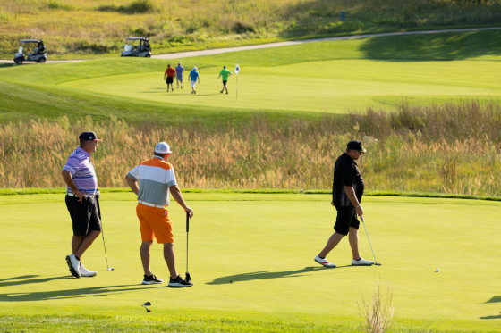 Three golfers appear in the foreground and four in the background at a golf fundraiser.