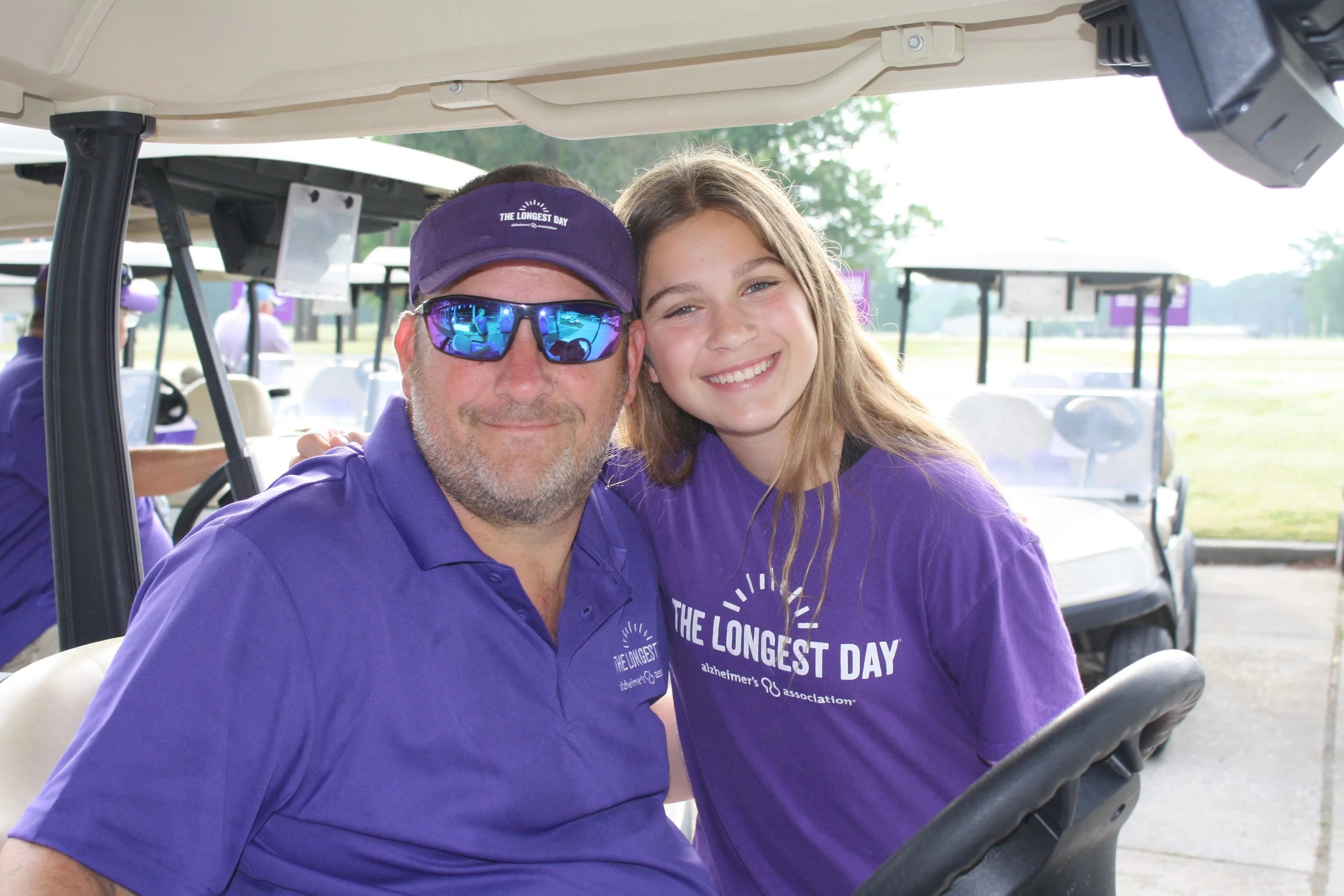 A man and a girl wearing purple shirts at a charity golf tournament organized by a chaptered nonprofit.
