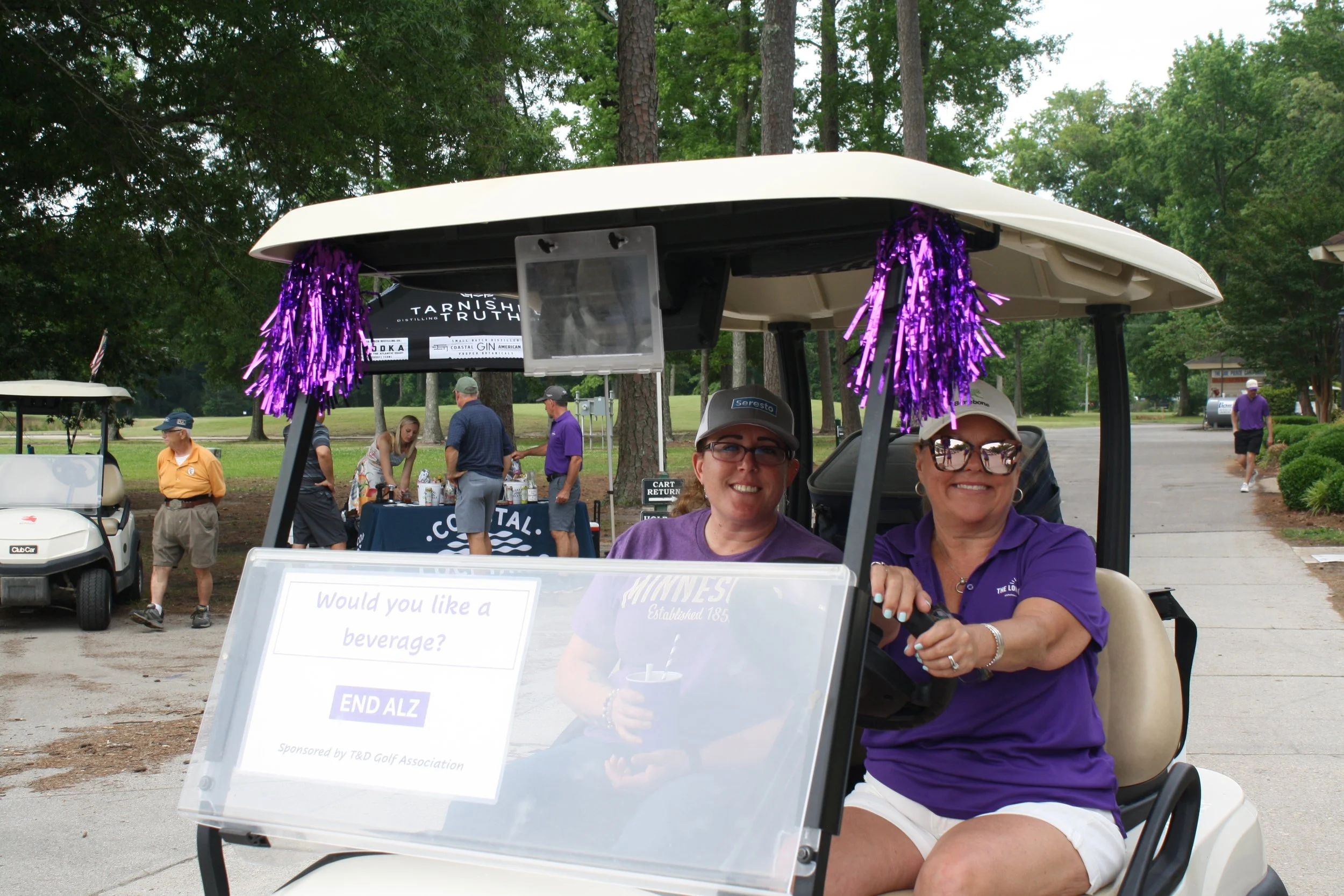 Two women drive a golf cart at a charity golf tournament organized by a chaptered nonprofit.