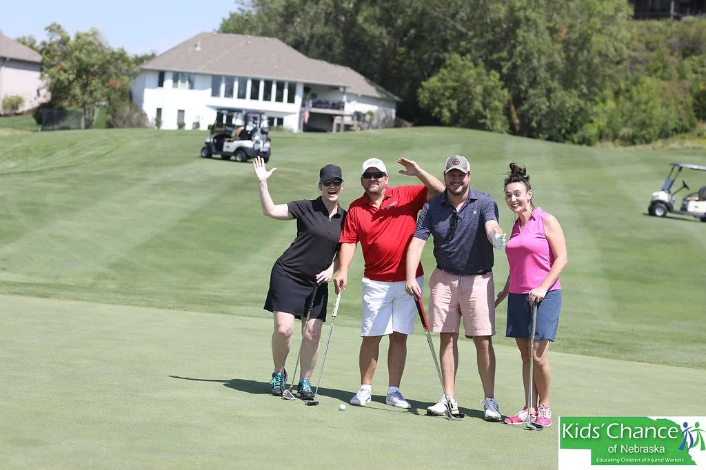 Two female and two male golfers post on a golf course at a golf fundraiser.