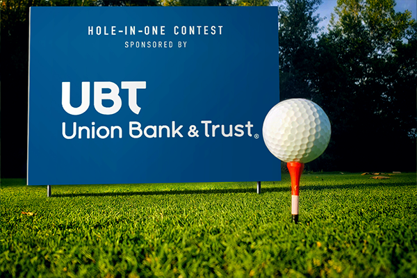 A sign on a tee box promoting the hole-in-one contest sponsor at a charity golf tournament.