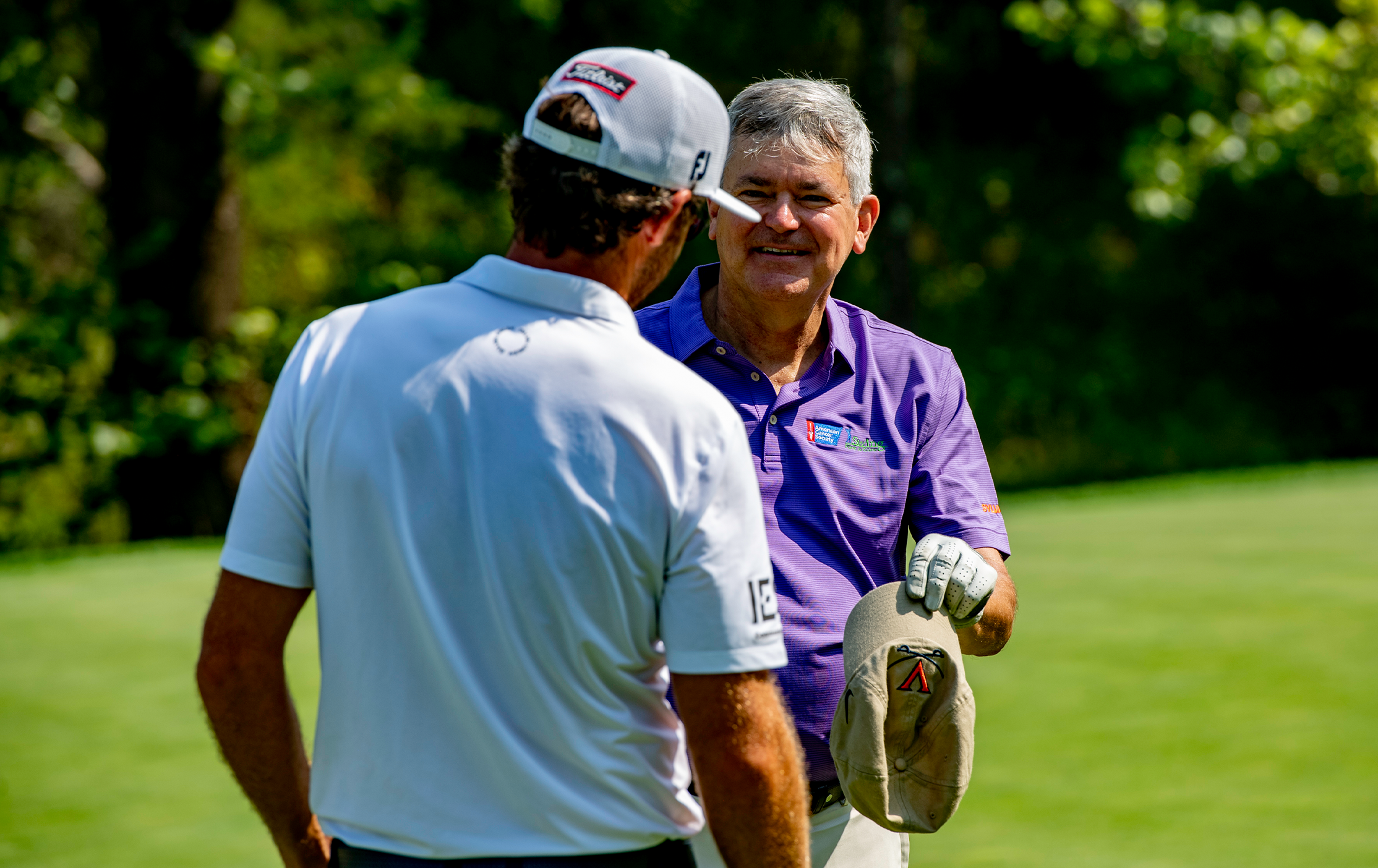 Two golfers shake hands at a charity golf event.