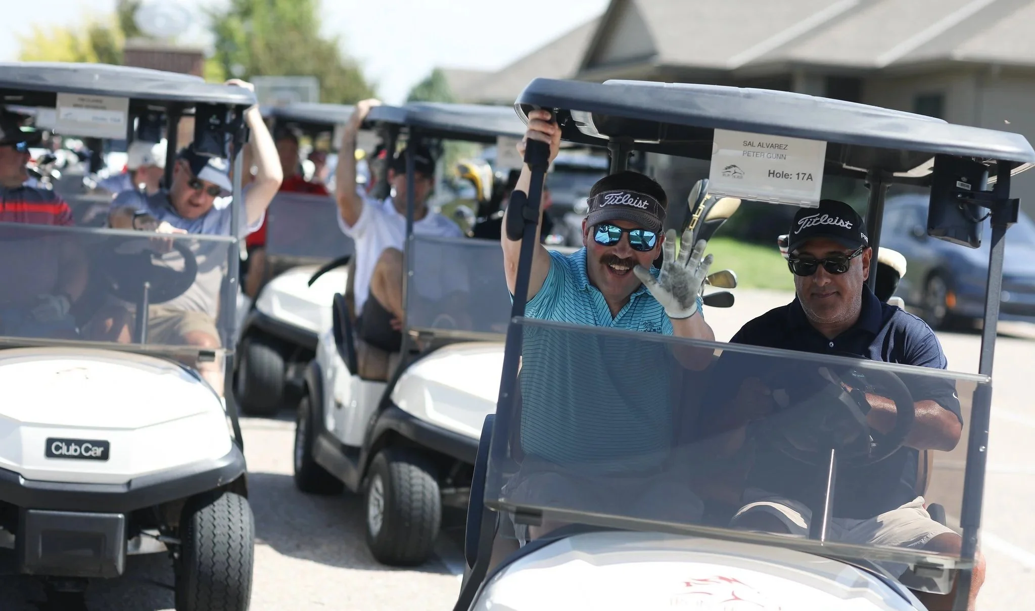 Golfers in a golf cart wave during a charity golf tournament.