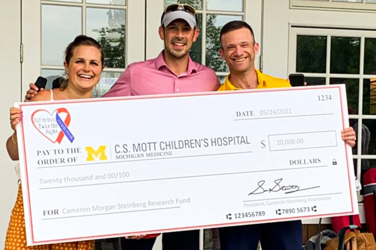 Three people hold a large check with money raised from a charity golf tournament.