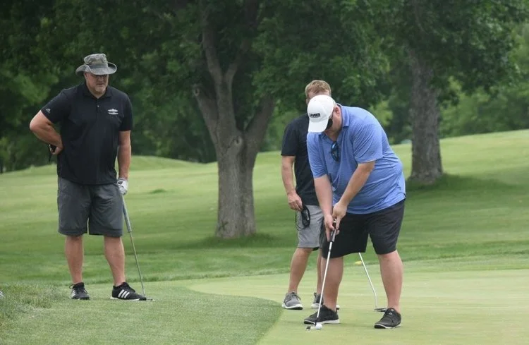 A man putts at a charity golf tournament while wearing a sleep shade.