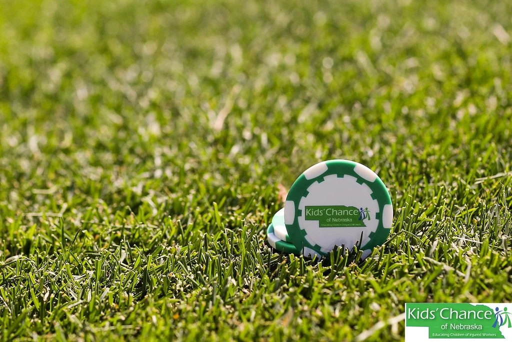 A Kids' Chance of Nebraska ball marker sits in the grass on a golf course.