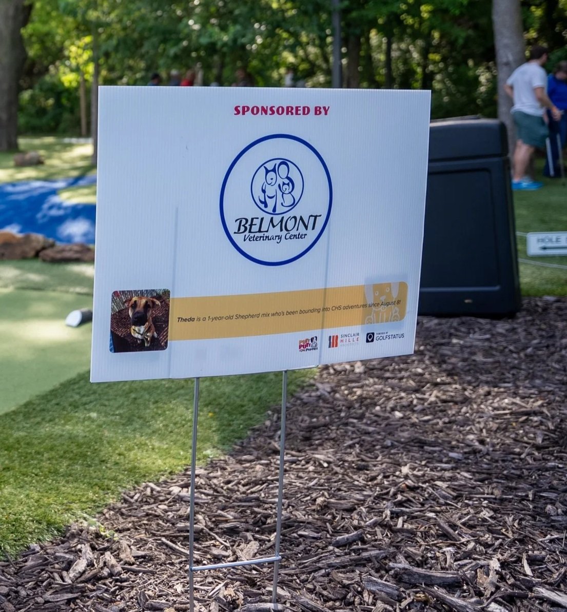 A hole sign with information about an adoptable dog is displayed at a charity golf tournament as a mission moment.
