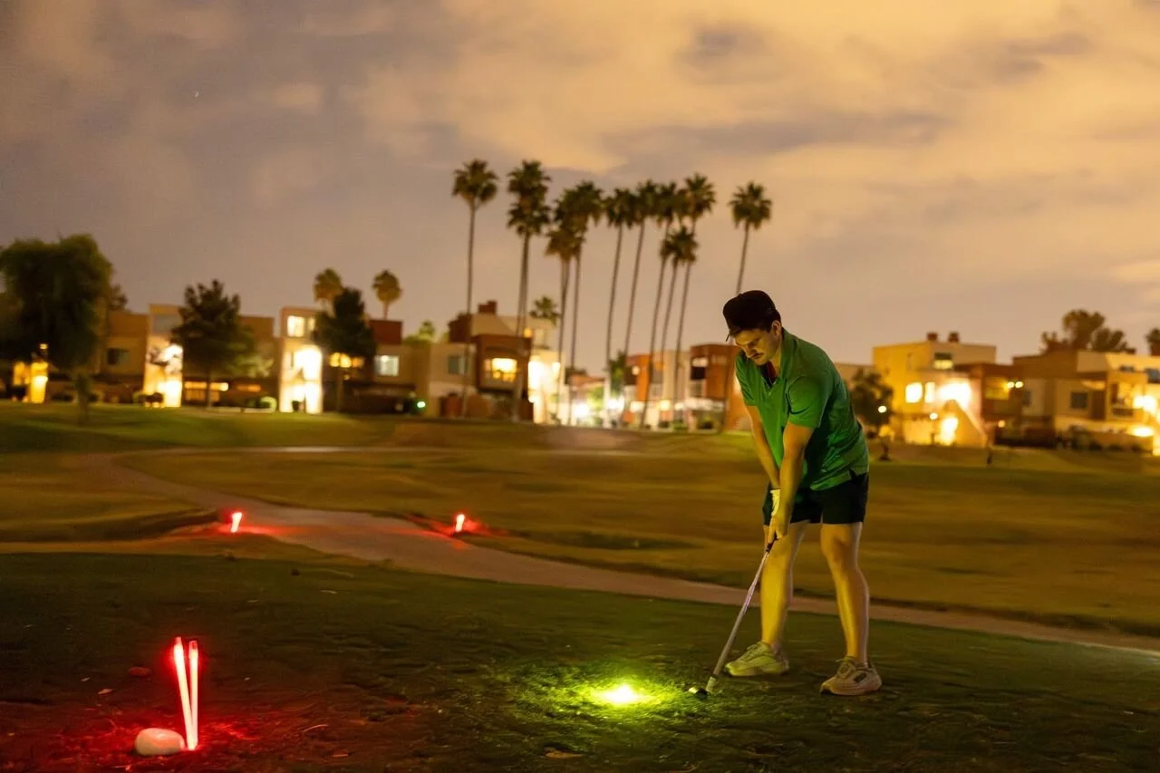 A golfer lines up to hit a glow-in-the-dark golf ball as part of a glow golf-themed tournament.