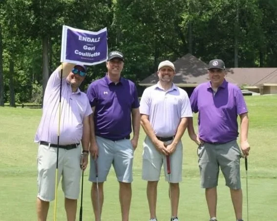 Four golfers stand next to a purple custom pin flag at a charity golf tournament.