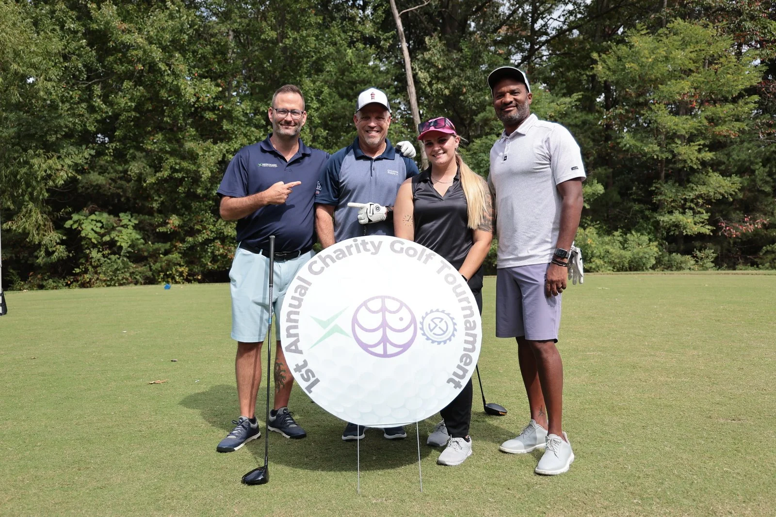 Three men and one woman golfer pose on the green at a charity golf event.
