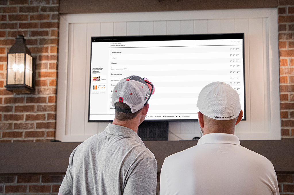 Two men view live leaderboards at a charity golf tournament.