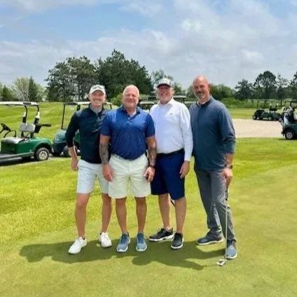 Four male golfers pose on a golf course at a charity golf tournament.