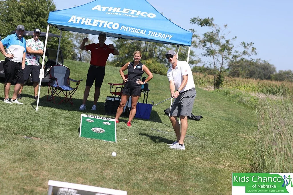 A golfer hits a ball toward a target at a sponsor tent at a charity golf tournament.
