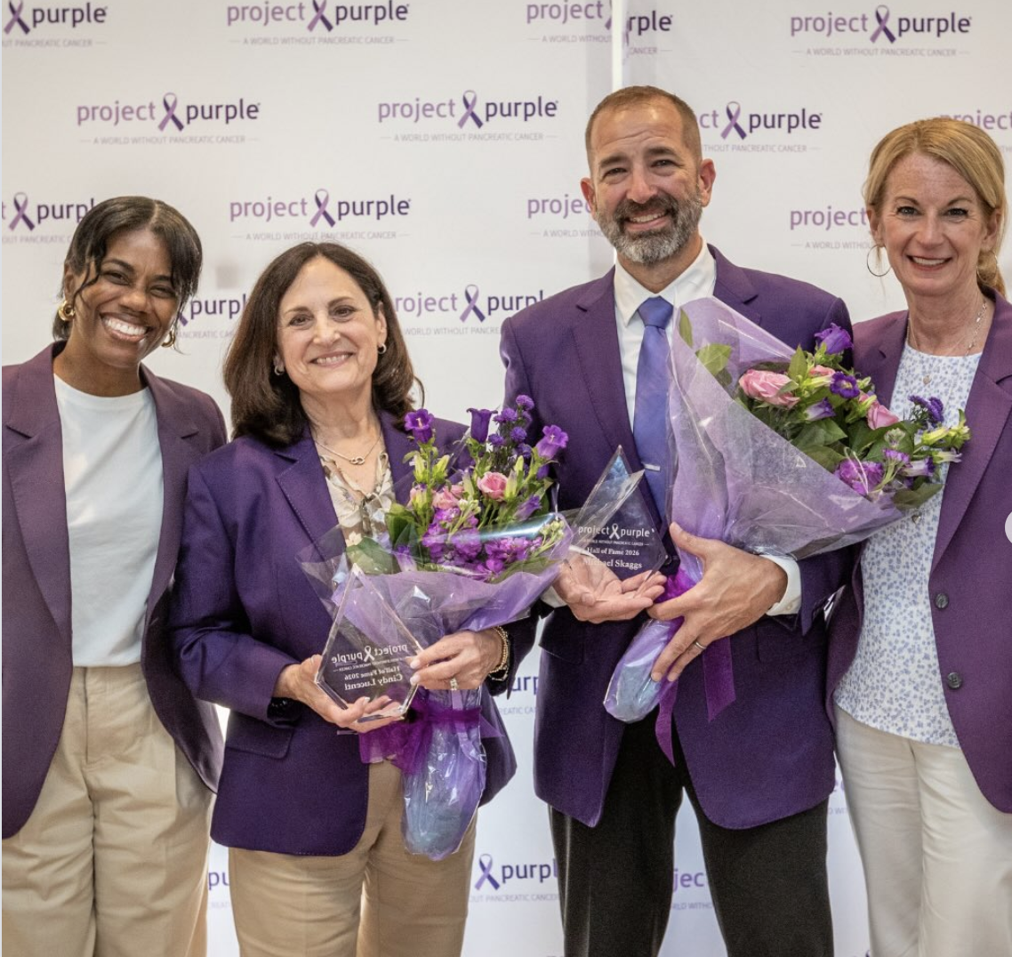 People dressed in purple jackets pose at a ceremony following a charity golf tournament.