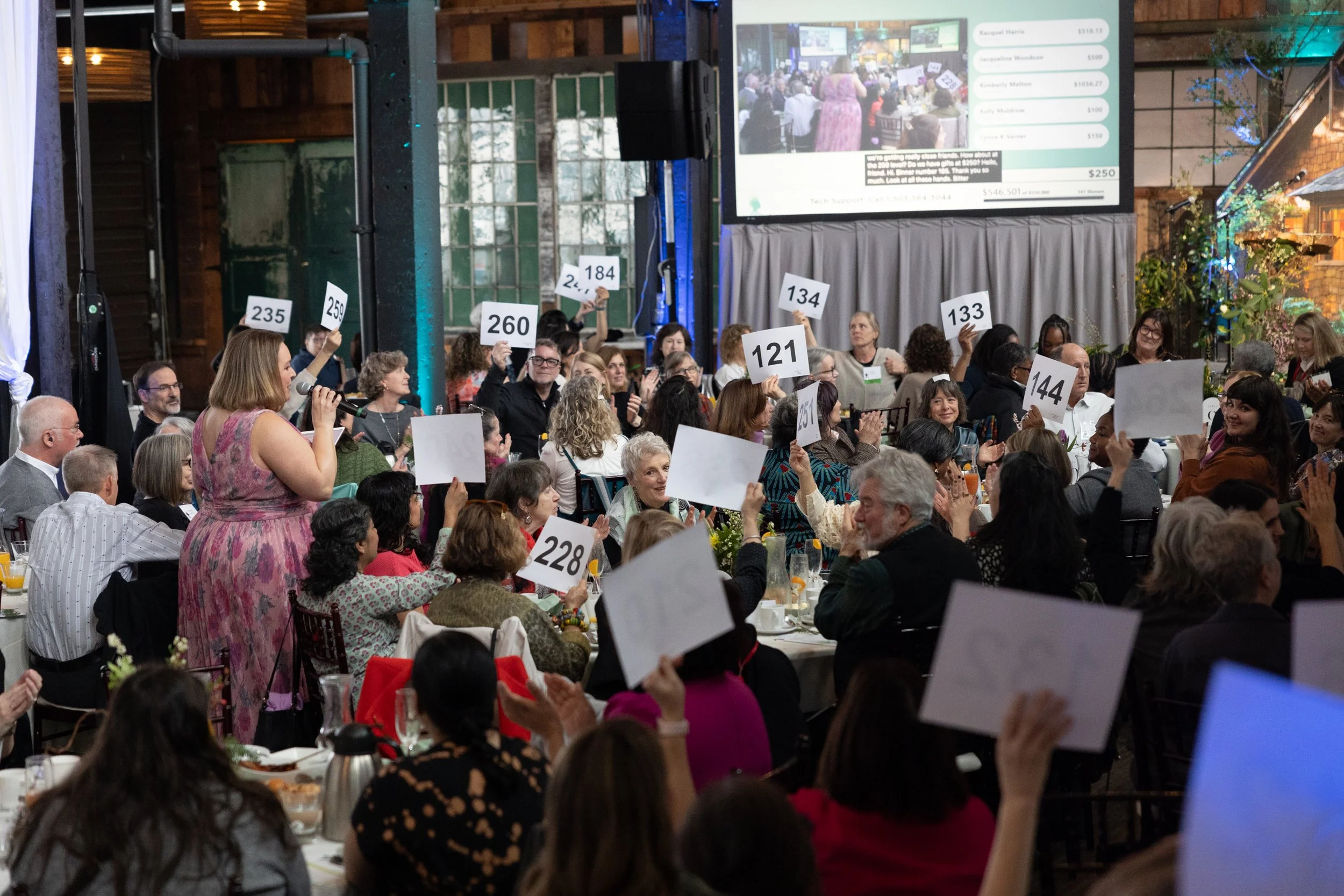 People seated at tables raise numbers as part of a fundraising event.