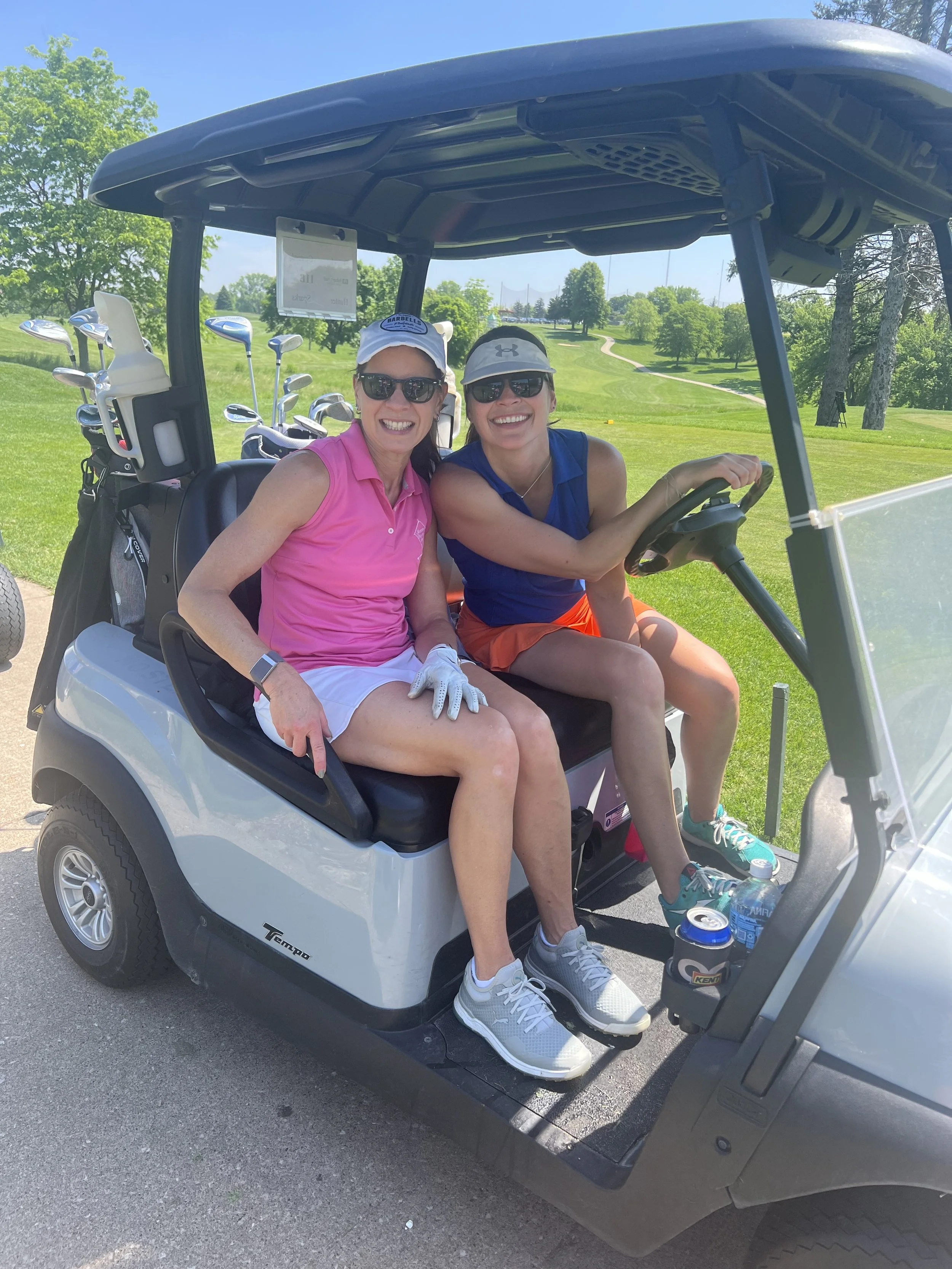 Two female golfers smile as they sit in a golf cart during a charity scramble.