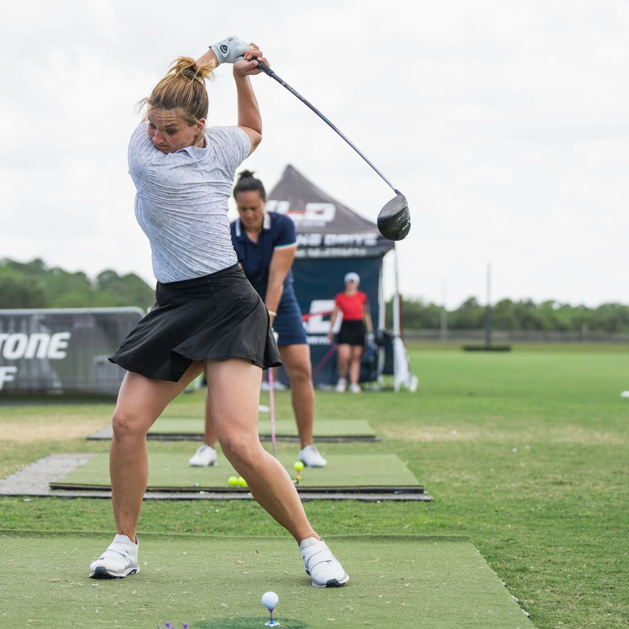 A female long-drive professional prepares to hit a tee shot at a golf event.