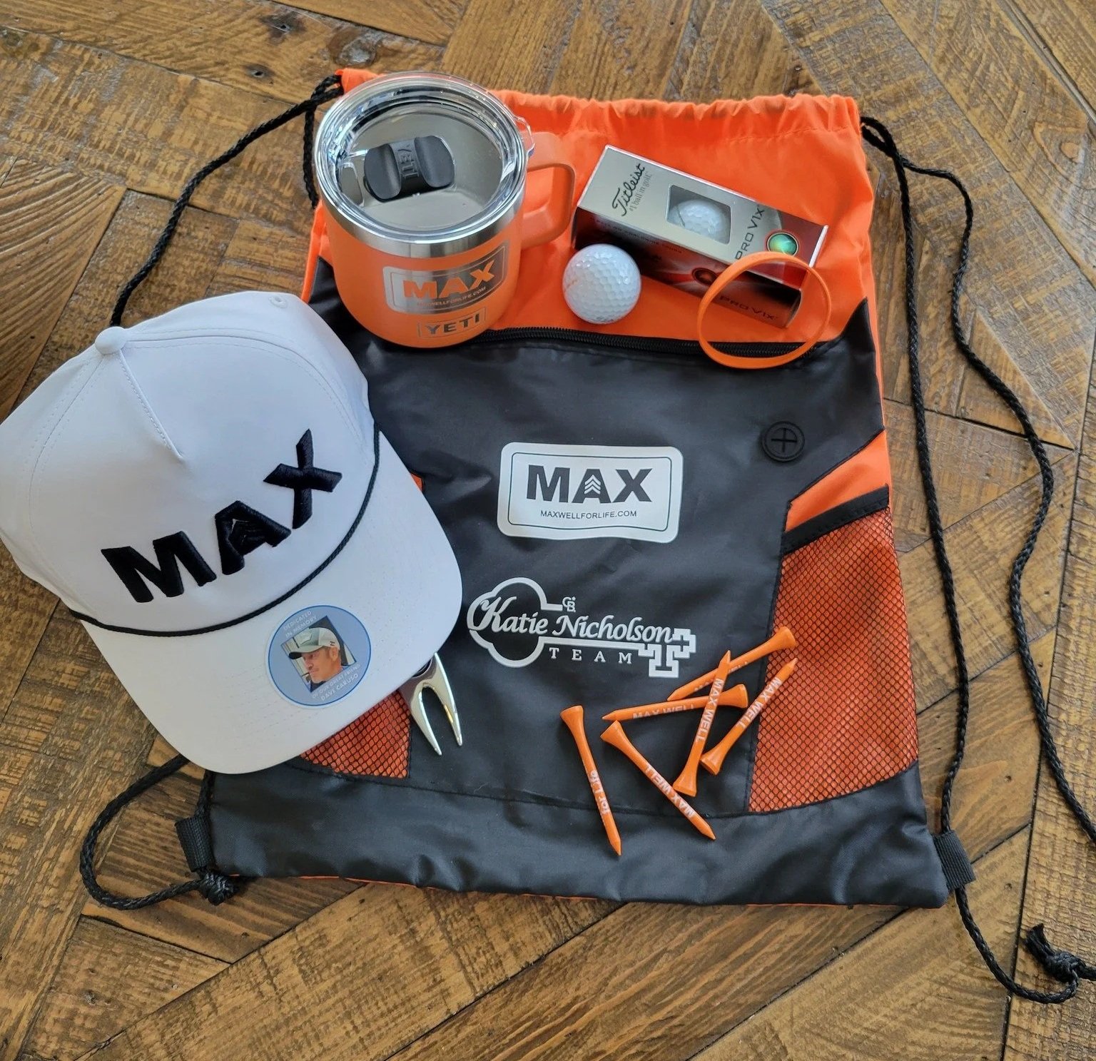 Player gifts from a charity golf tournament, including a hat, mug, golf balls, tees, and bag.