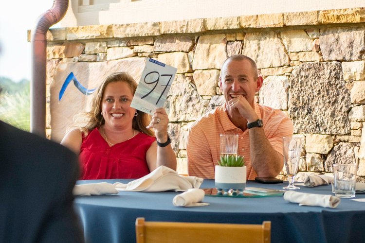 A women bids on an item at a golf charity auction.