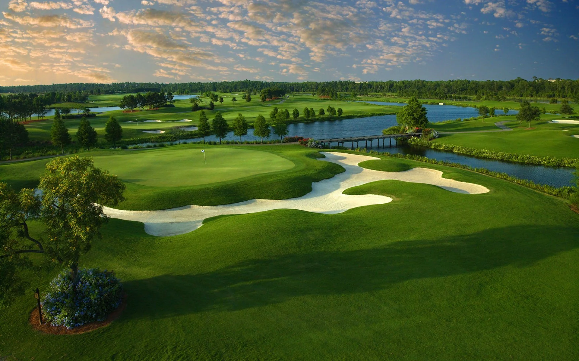 A golf course with a green in the foreground and water features in the background.